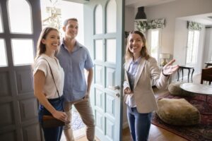 Positive, real estate agent welcoming young married couple into house for sale or renting